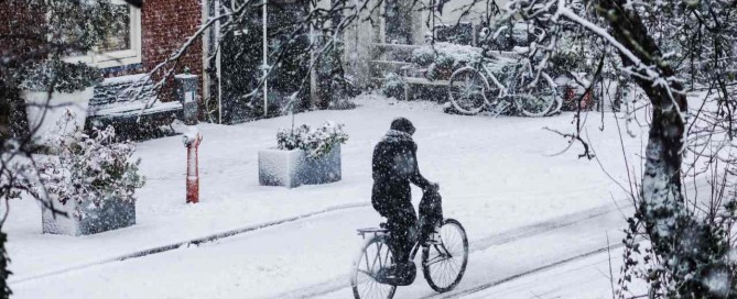 Frau auf Fahrrad fährt durch den Schnee.